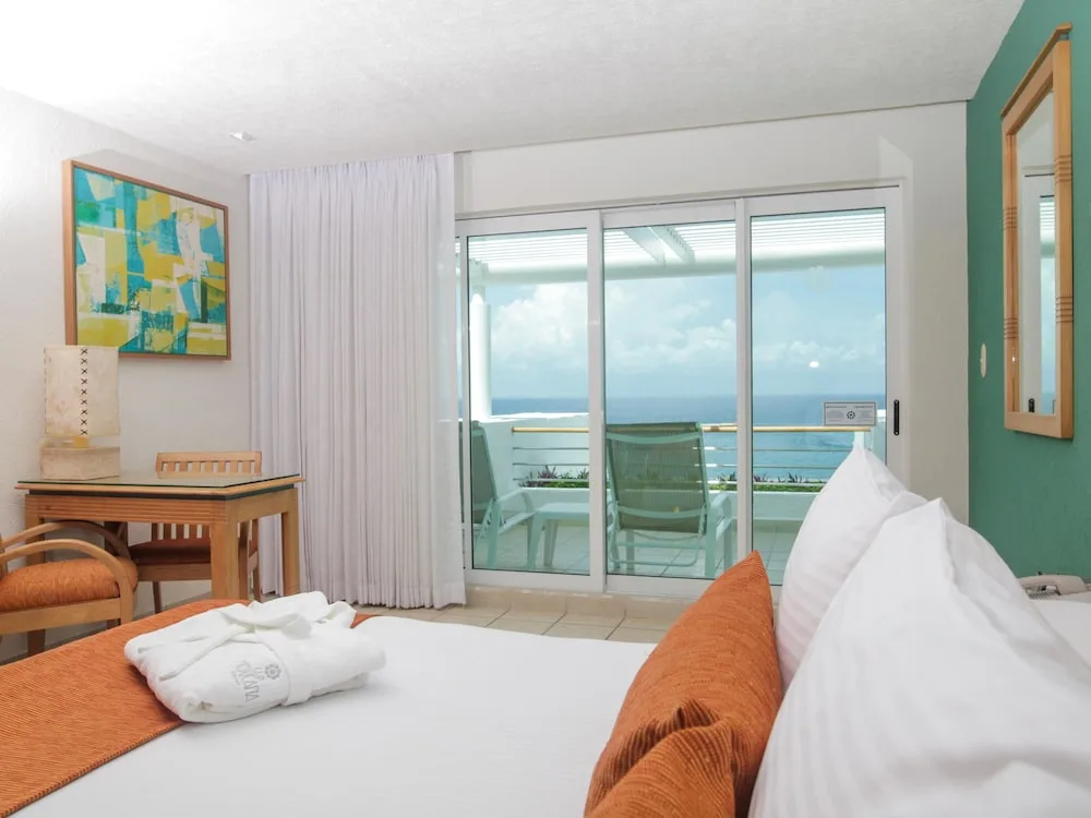 Guest room with king bed and sliding balcony doors showing ocean at Casa Mexicana Cozumel