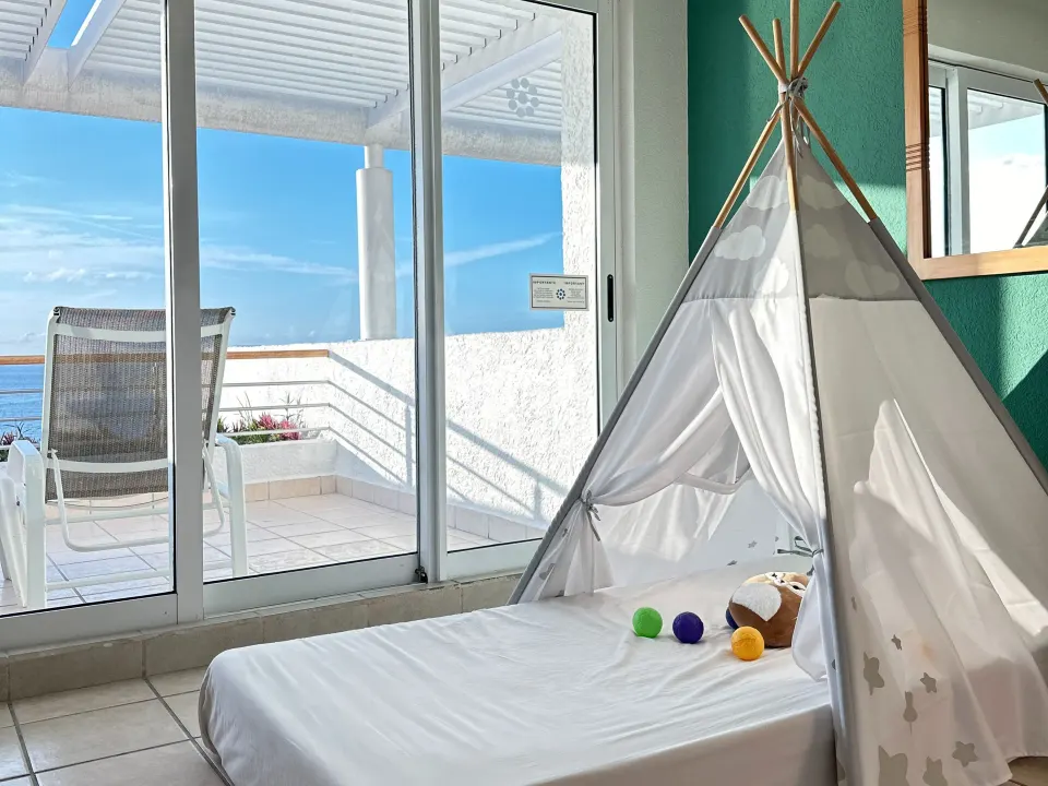 Guest room with children's teepee on the floor and sliding doors to a balcony with ocean glimpses at Casa Mexicana Cozumel.