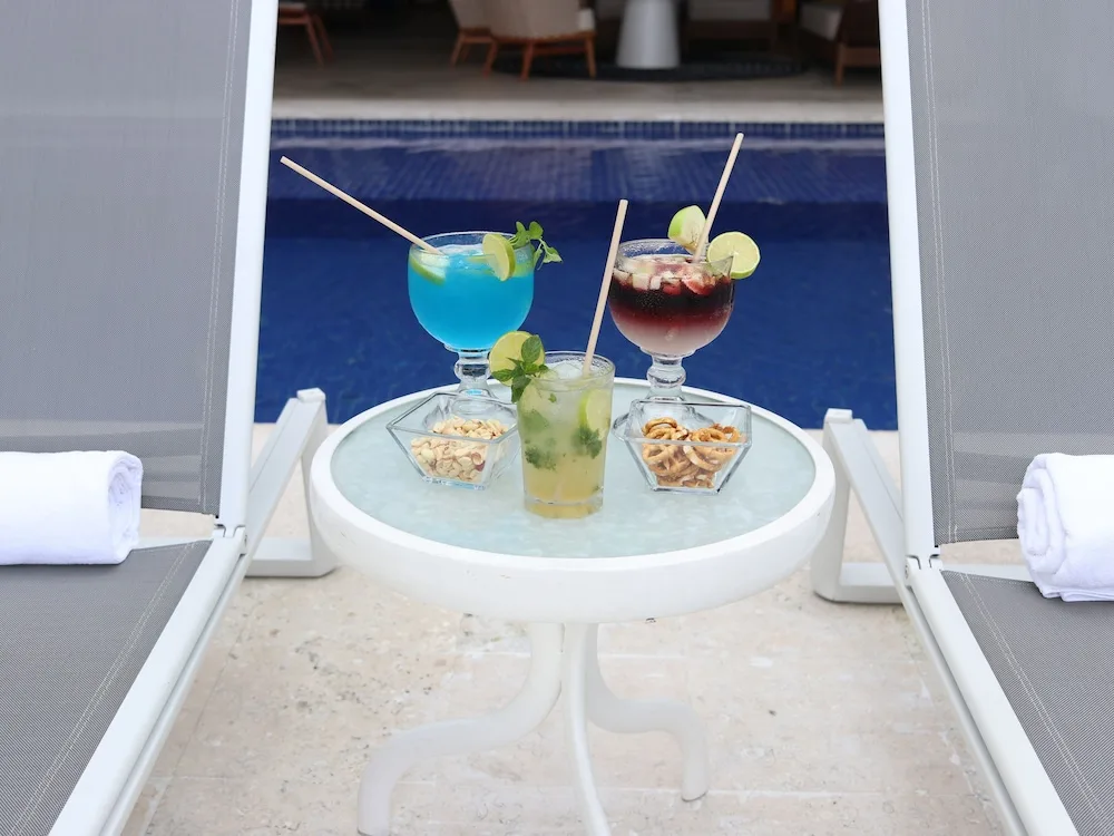 Three cocktails and snacks on a small table between pool loungers at Casa Mexicana Cozumel