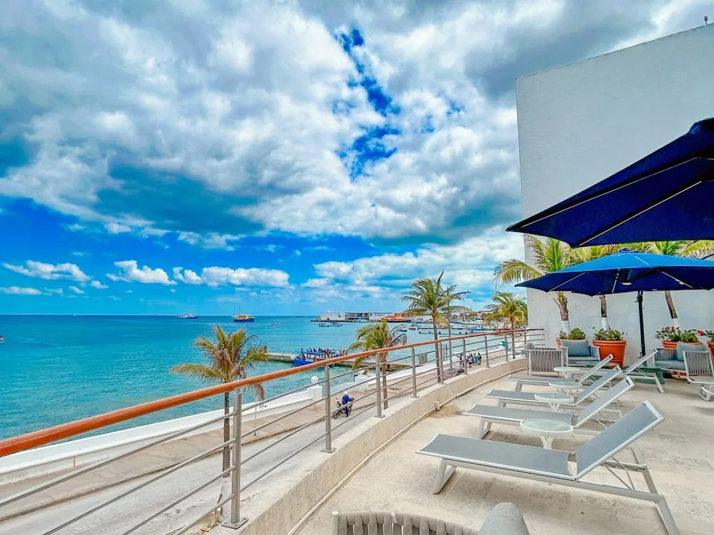 Oceanfront terrace with loungers, umbrellas and palm trees at Casa Mexicana Cozumel