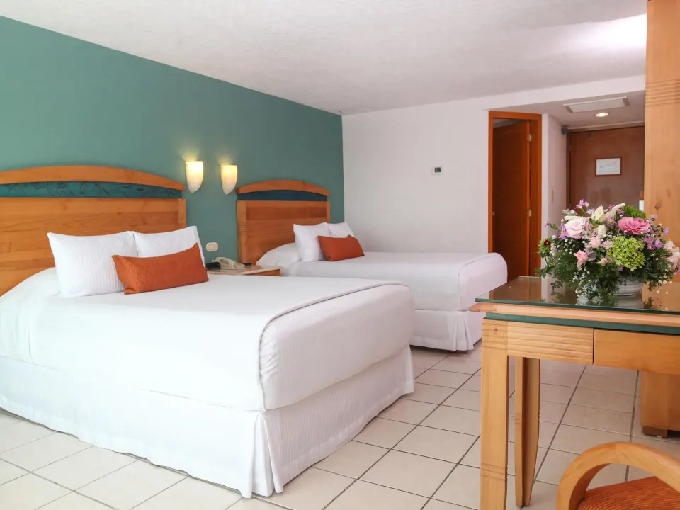 Guest room with two double beds, green accent wall and desk at Casa Mexicana Cozumel.
