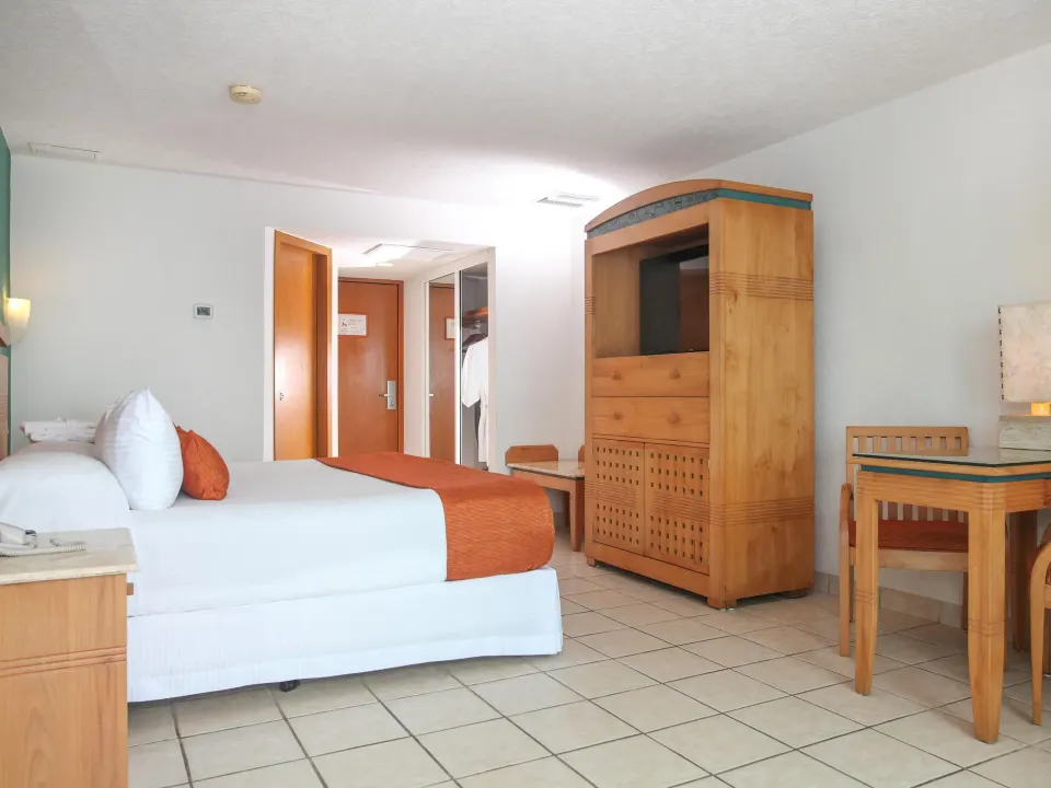 Wide view of a Habitacion Deluxe showing bed, desk and TV cabinet at Casa Mexicana Cozumel