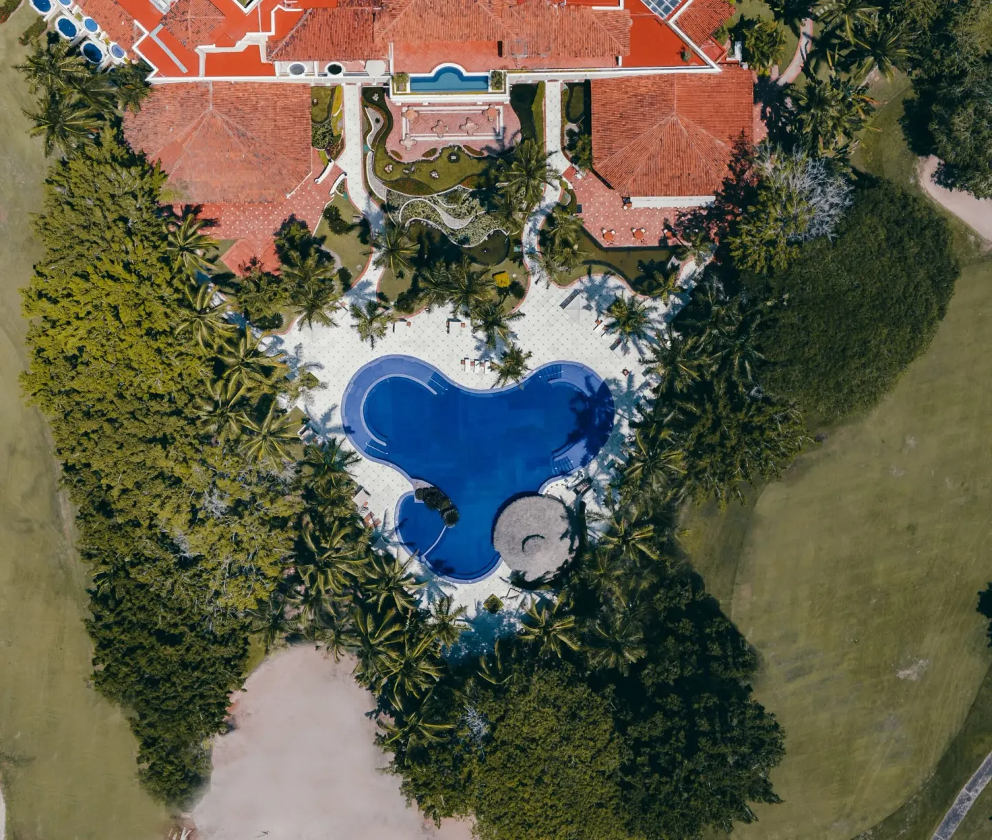 An aerial view shows the curved pool, palms, and red-tile roofs at Casa Velas.