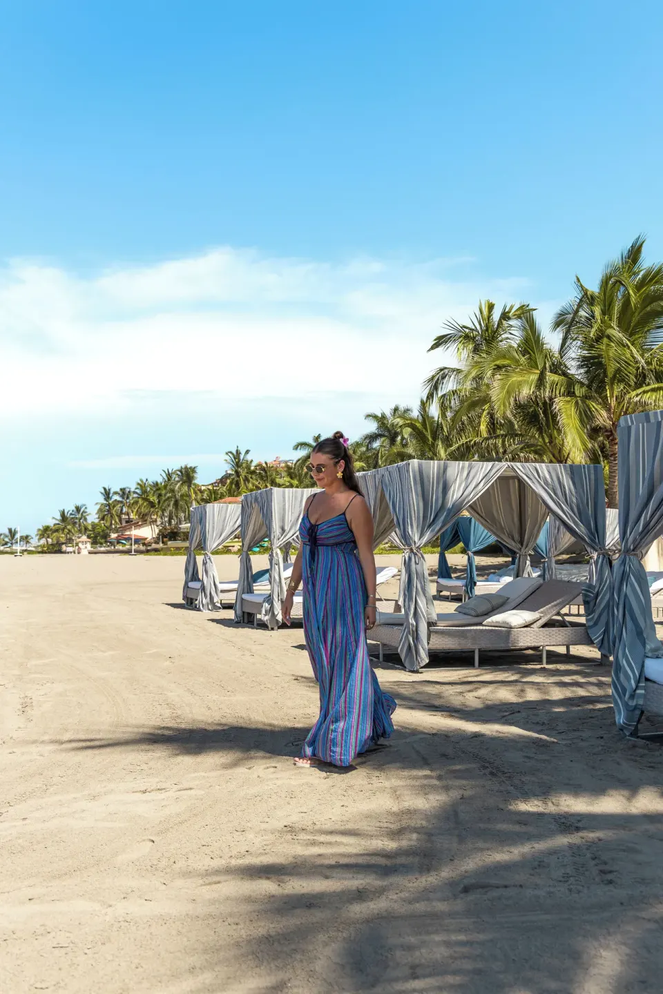 Beach cabanas and loungers line the sand as a guest walks at Casa Velas.