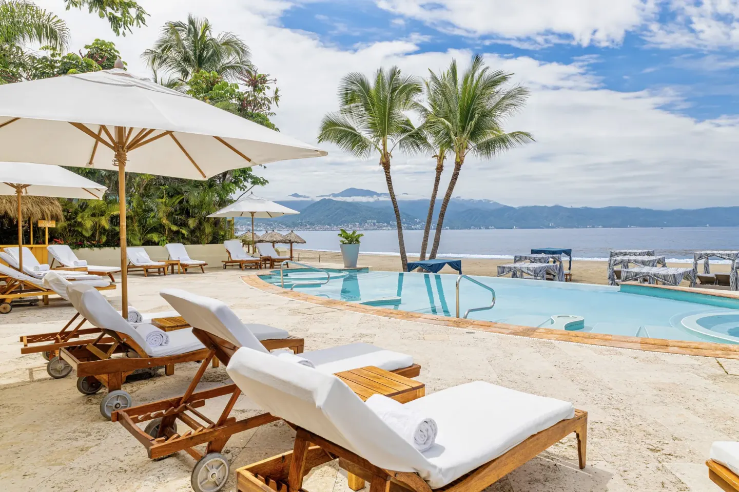 Beachfront pool with loungers, umbrellas, palms, and ocean view at Casa Velas.