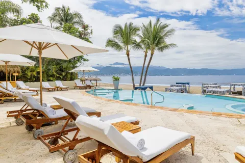 Beachfront pool with loungers, umbrellas, palms, and ocean view at Casa Velas.