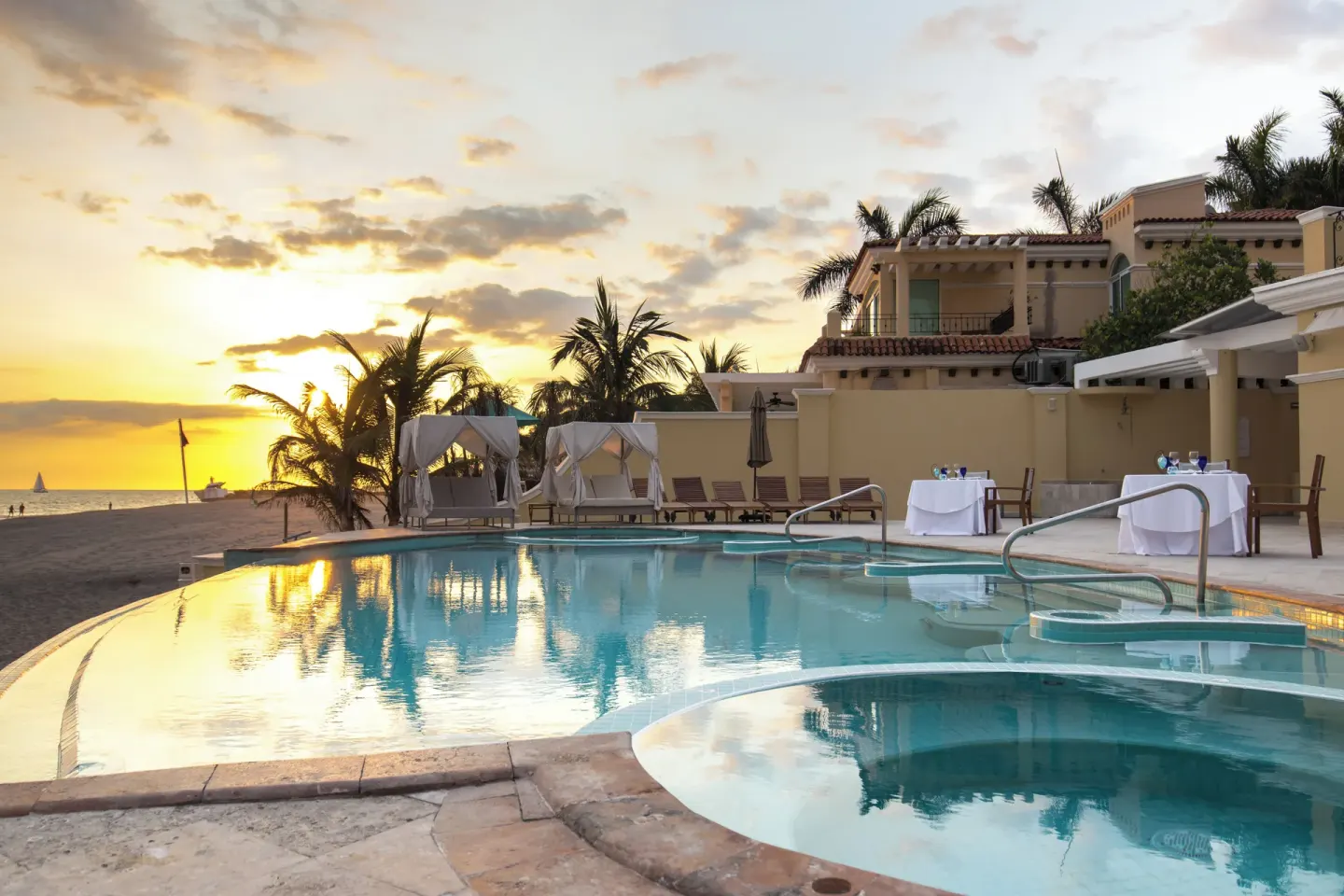 Beachfront pool with cabanas, dining tables, and sunset sky at Casa Velas.