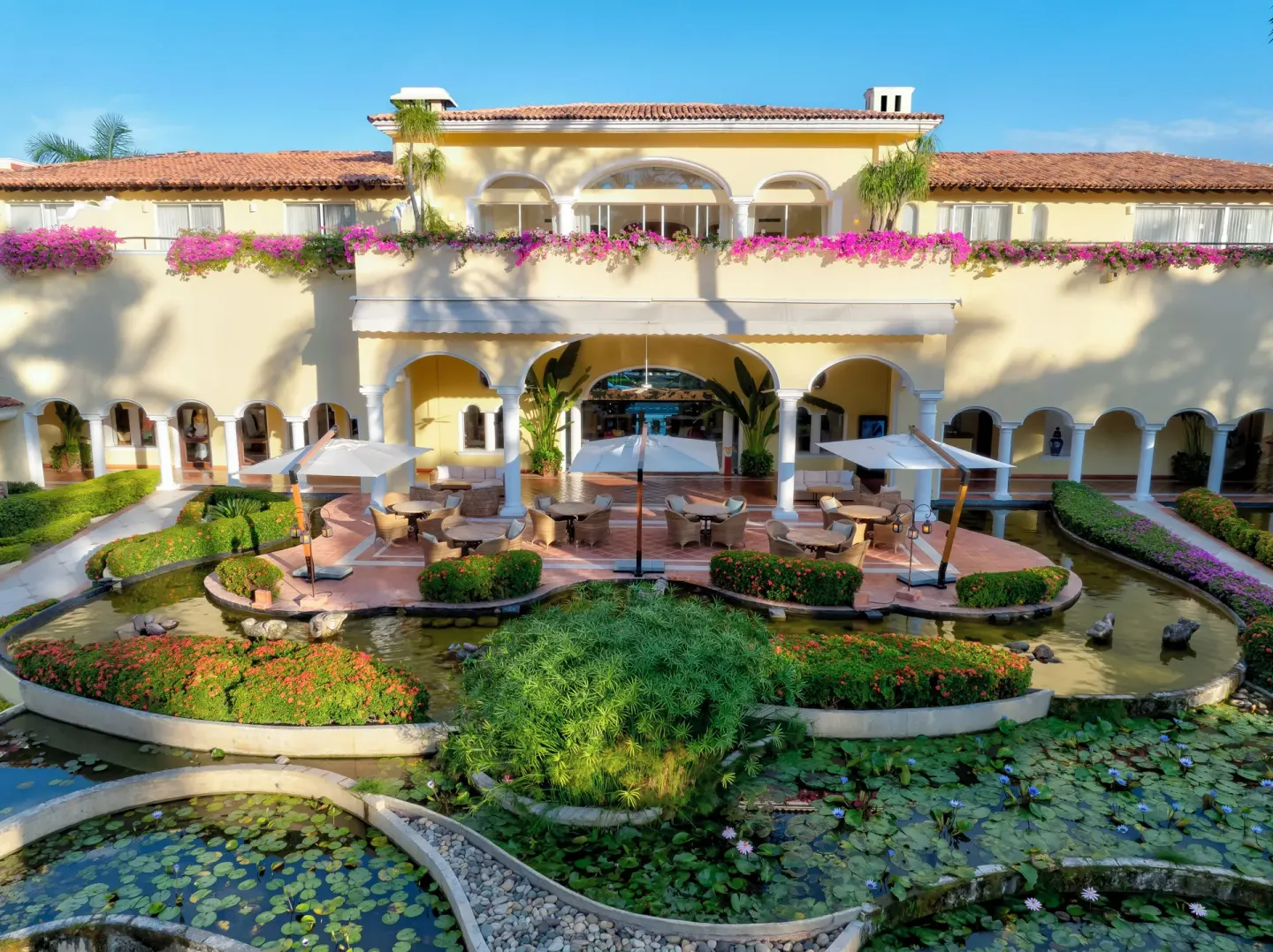 Courtyard with arched terraces, umbrellas, ponds, and flowers at Casa Velas.