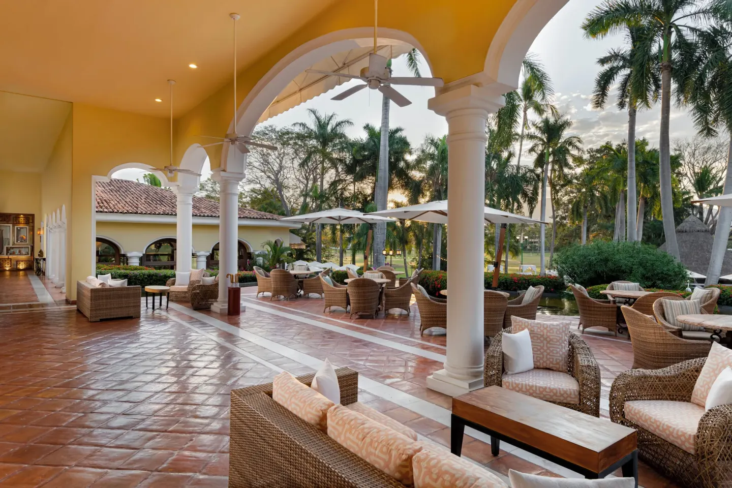 Covered terrace with wicker seating, arches, and palm garden views at Casa Velas.