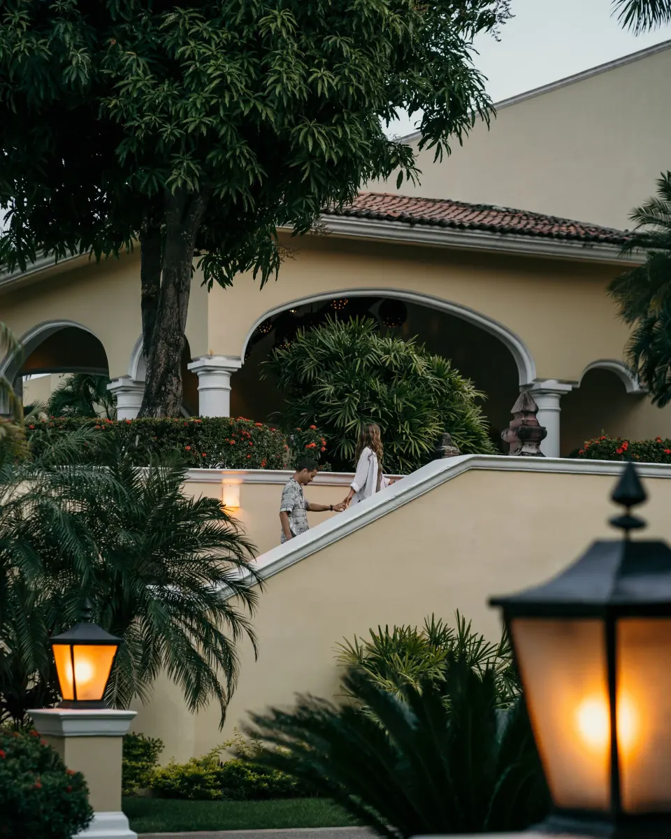 Two guests walk along a garden stairway beside arched architecture at Casa Velas.