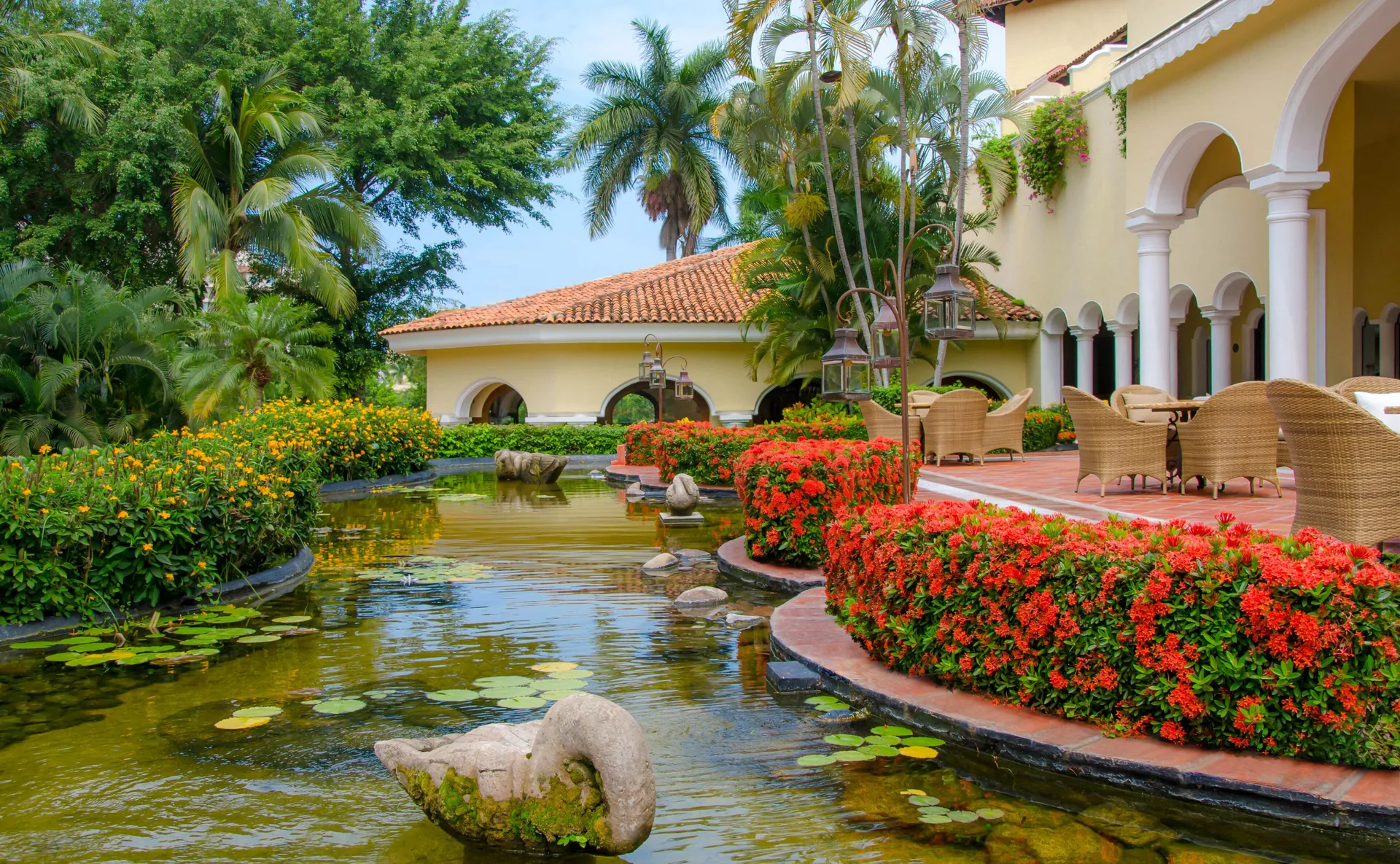 A lily pond and terrace with wicker chairs sit beside arched buildings at Casa Velas.