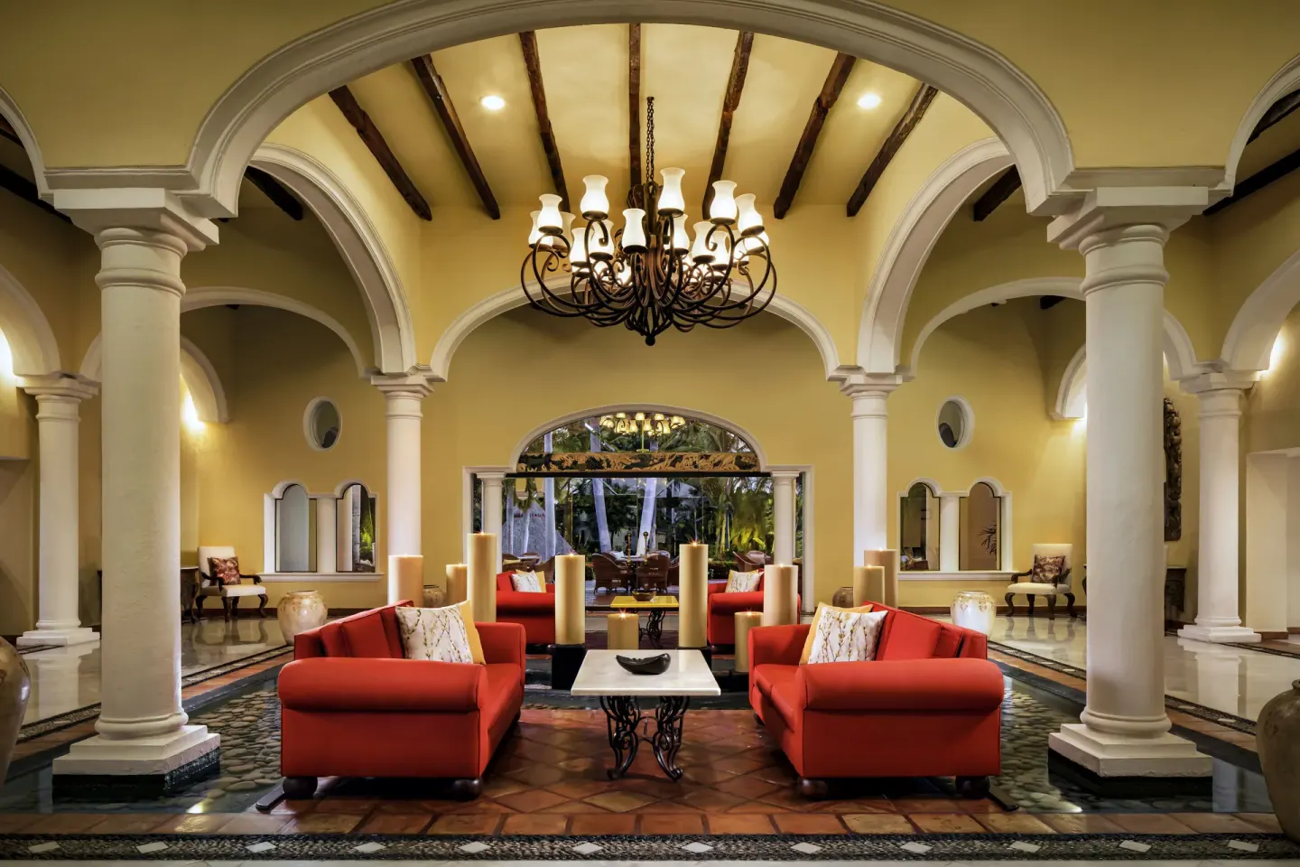 Lobby lounge with red sofas, arches, columns, and chandelier at Casa Velas.