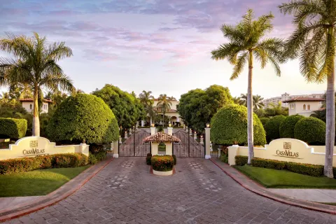 The gated entrance to Casa Velas is framed by palms, hedges, and resort signs.