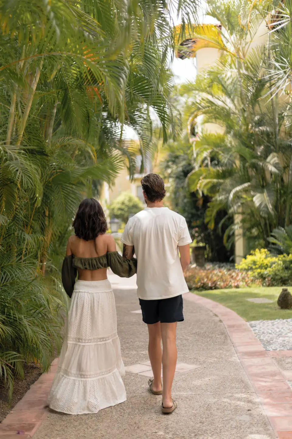 Couple walking along a palm-lined garden path at Casa Velas.