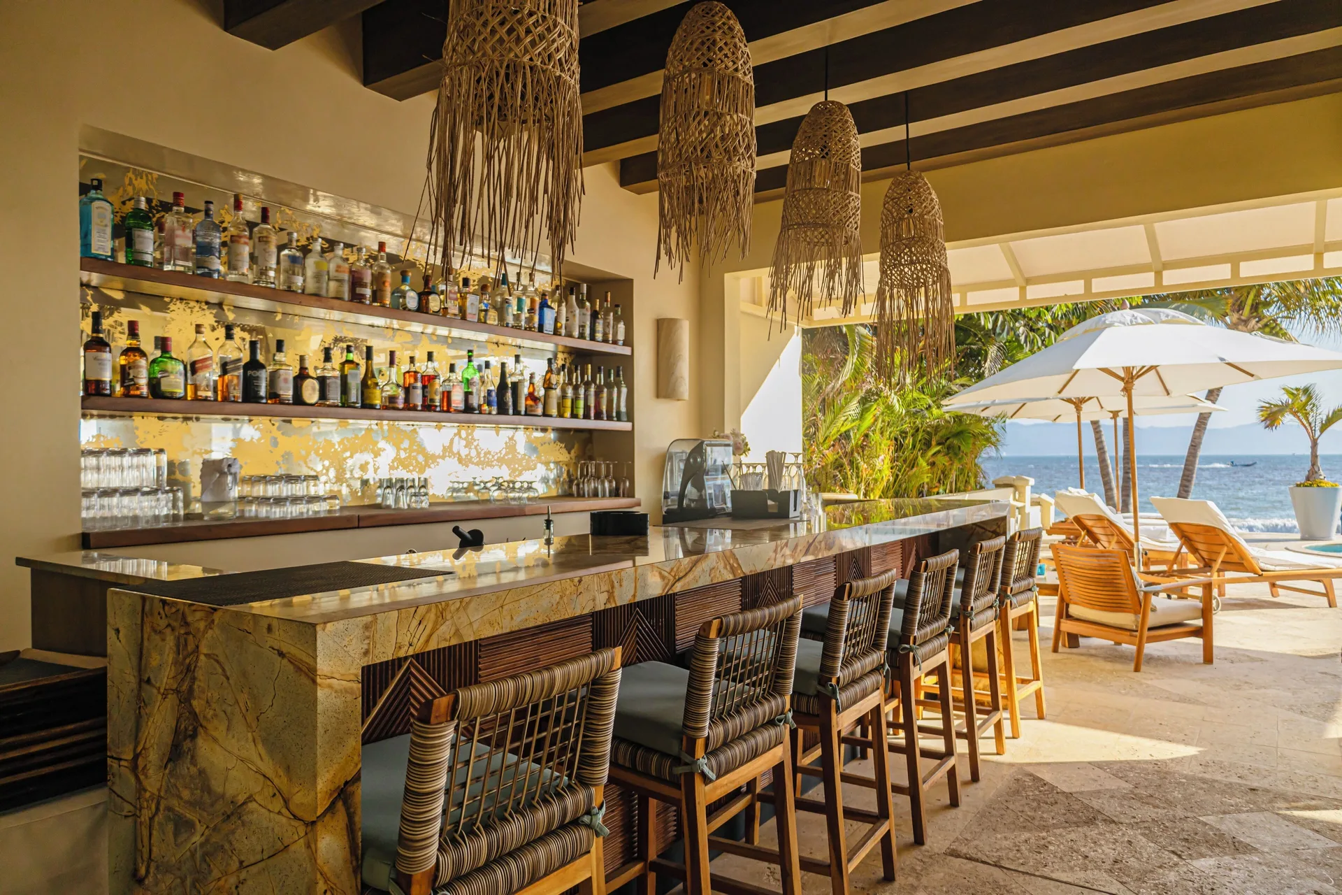 Beach club bar with stools, bottles, and ocean views at Casa Velas.