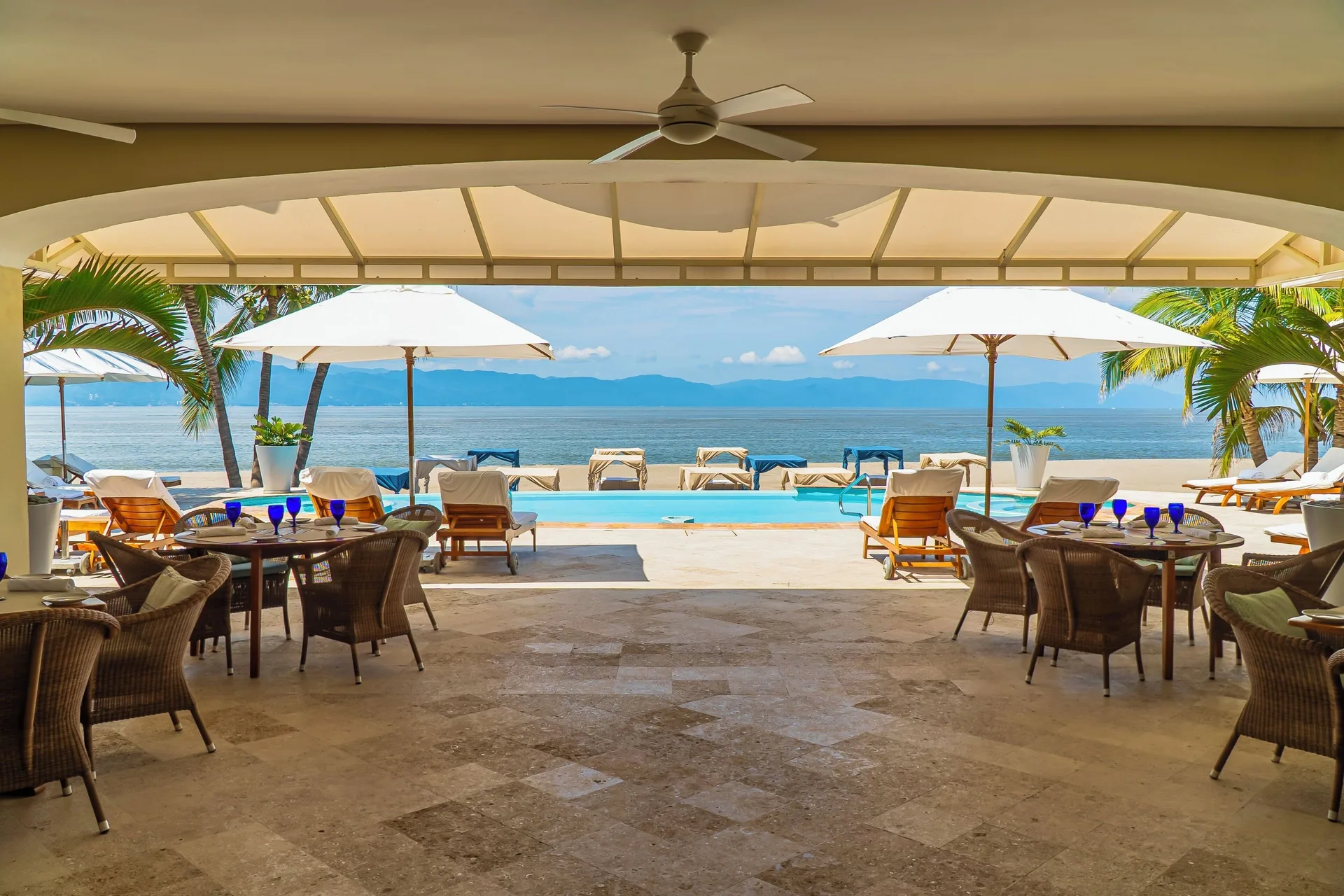 Beach club terrace with dining tables, pool loungers, and ocean view at Casa Velas.