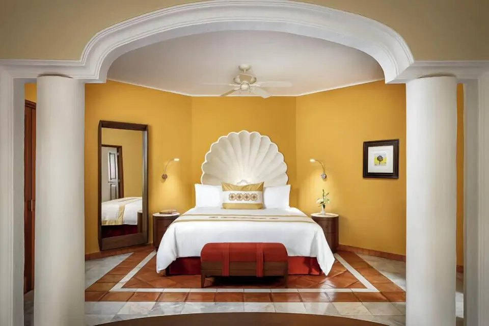 Master Suite king bed at Casa Velas framed by columns, a scalloped headboard, and yellow walls.