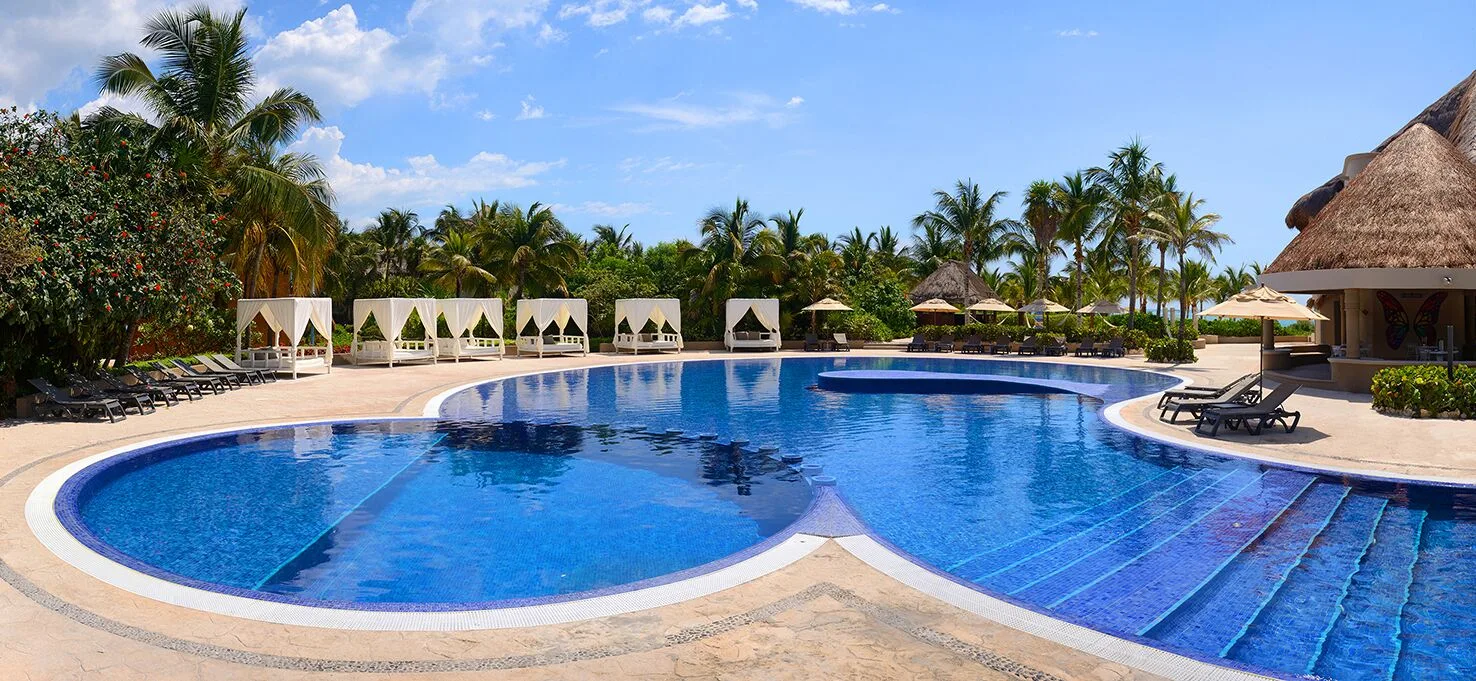 Curved resort pool with cabanas and palms at Catalonia Playa Maroma.