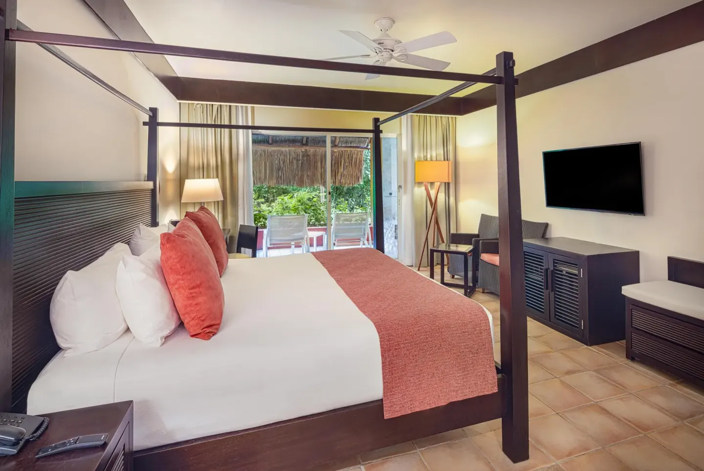 Guest room with four-poster king bed, TV and patio doors at Catalonia Playa Maroma.