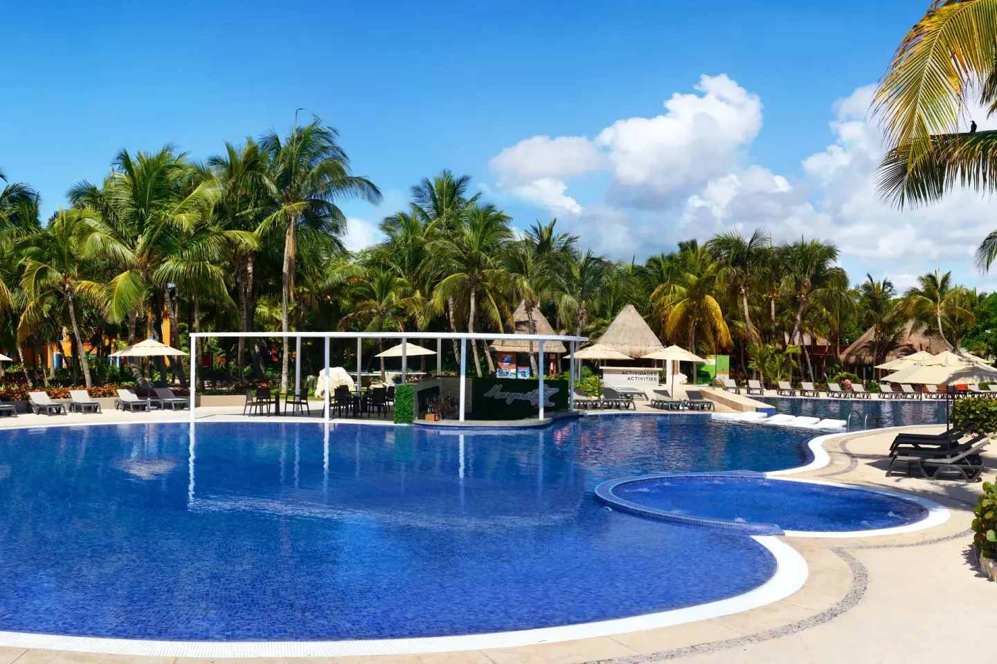 Large blue pool with an activity area and palm trees at Catalonia Playa Maroma.