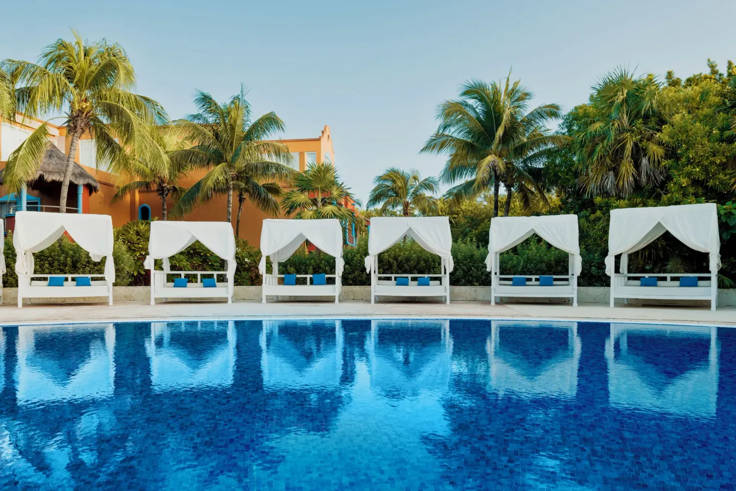 Poolside cabanas reflected in the water beside palms at Catalonia Playa Maroma.