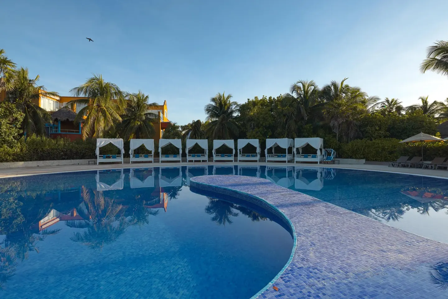 Quiet pool with a curved tiled walkway and cabanas at Catalonia Playa Maroma.