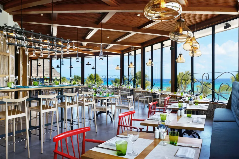 Bright modern restaurant with floor-to-ceiling windows and bar at Catalonia Riviera Maya Resort and Spa