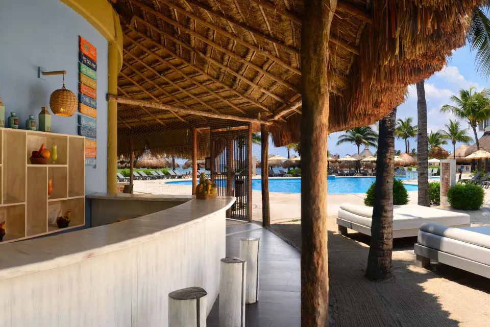 Thatched-roof pool bar with curved counter and lounge beds at Catalonia Riviera Maya Resort and Spa