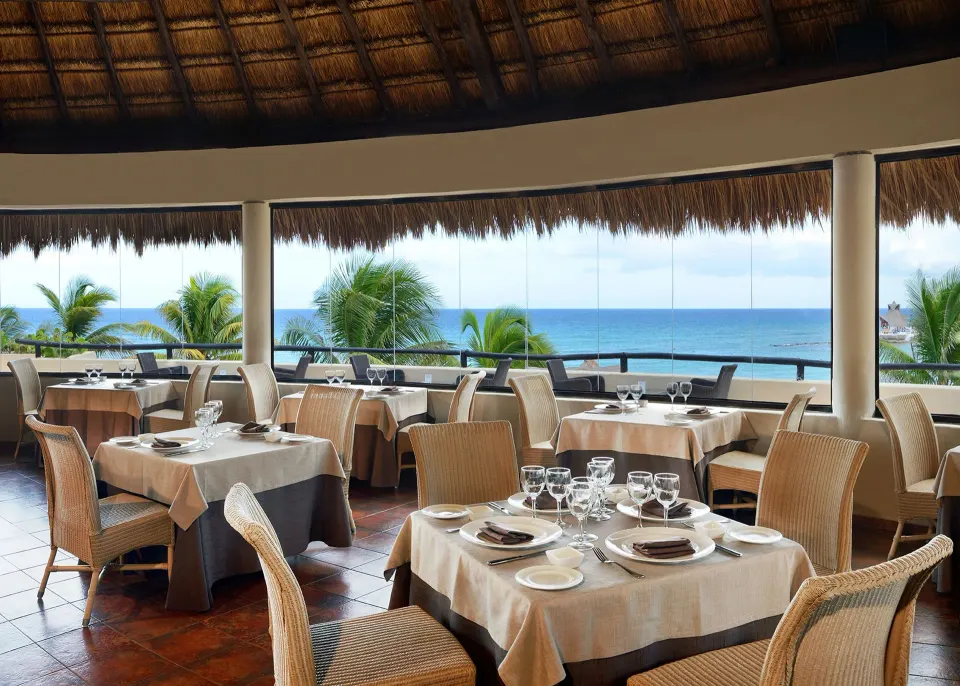 Thatched-roof beachfront restaurant with ocean view tables at Catalonia Riviera Maya Resort and Spa