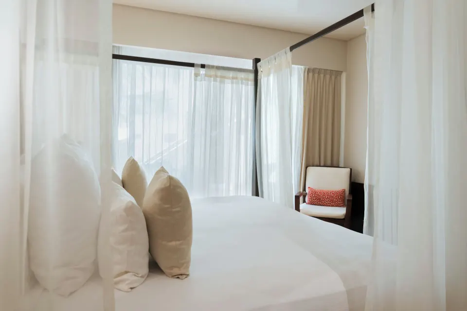 Four-poster king bed with sheer curtains and chair in a Privileged Romance Room at Catalonia Riviera Maya Resort and Spa