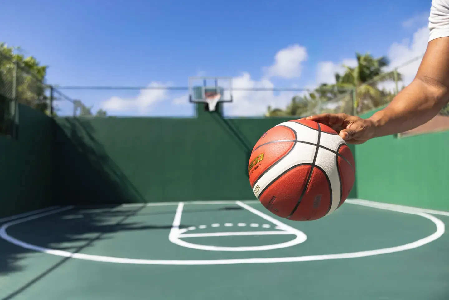 A hand holds a basketball on an outdoor court at Catalonia Royal Bavaro.