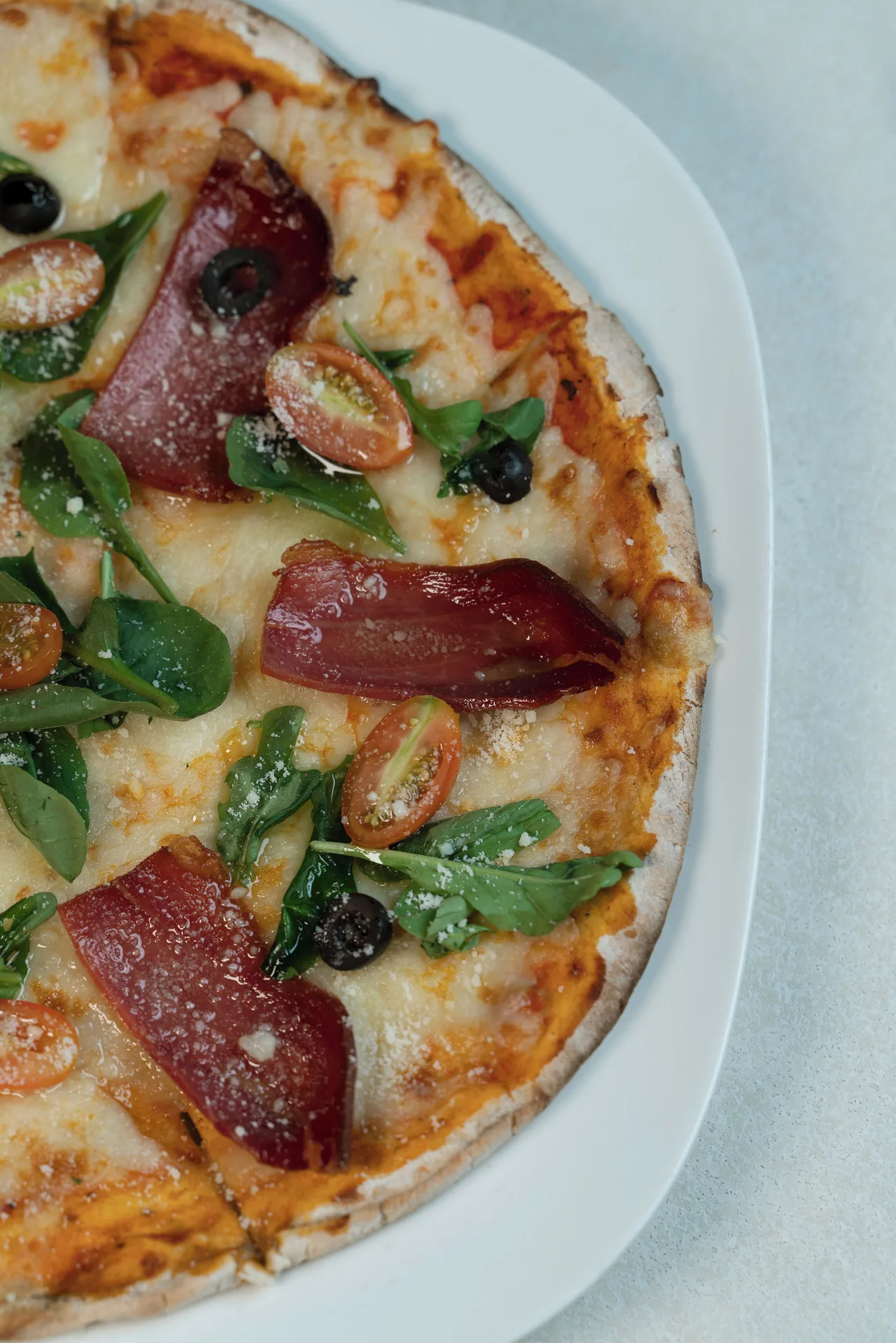 A close-up of pizza with tomatoes, greens, olives, and cured meat at Catalonia Royal Bavaro.