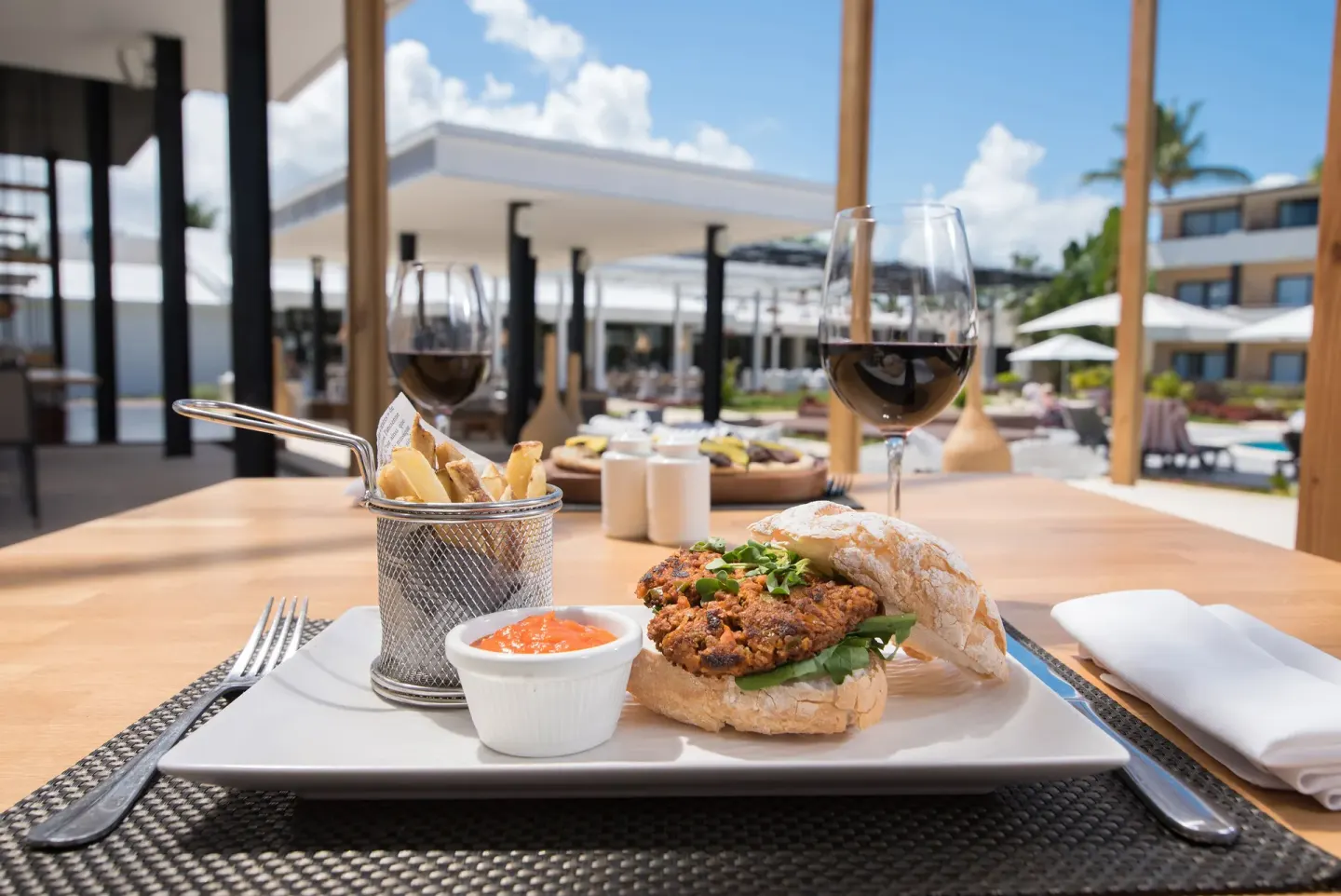 A burger, fries, sauce, and red wine are served on a terrace at Catalonia Royal Bavaro.