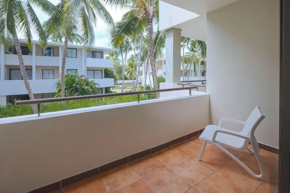 Privileged Deluxe Junior Suite balcony with chair and palm garden view at Catalonia Royal Bavaro.