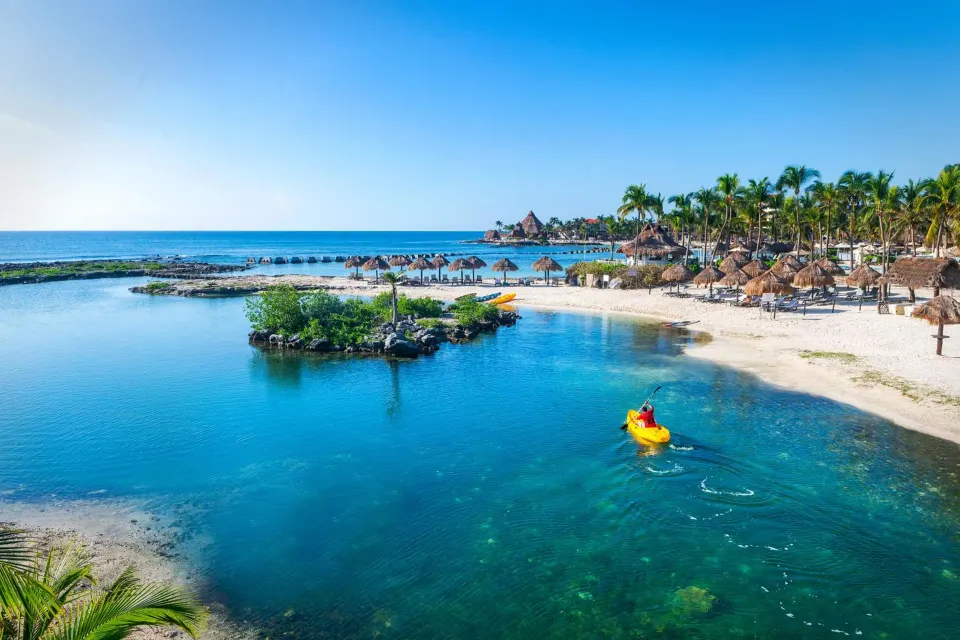 Resort beachfront lagoon with kayaker and palapas at Catalonia Yucatan Beach.
