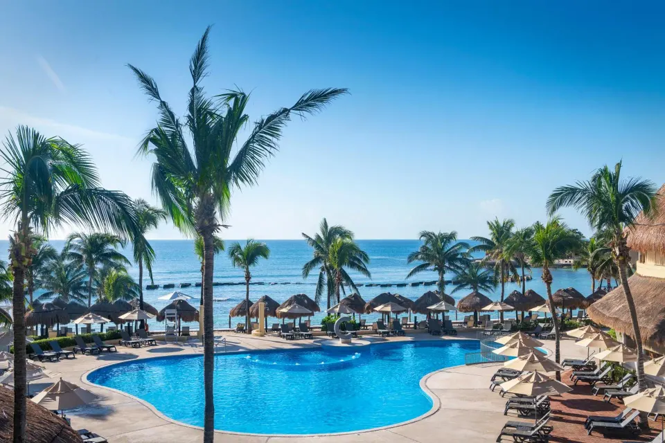 Resort pool with palm trees and ocean view at Catalonia Yucatan Beach.