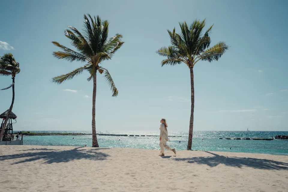 Person walking between palms on the sunlit beach at Catalonia Yucatan Beach