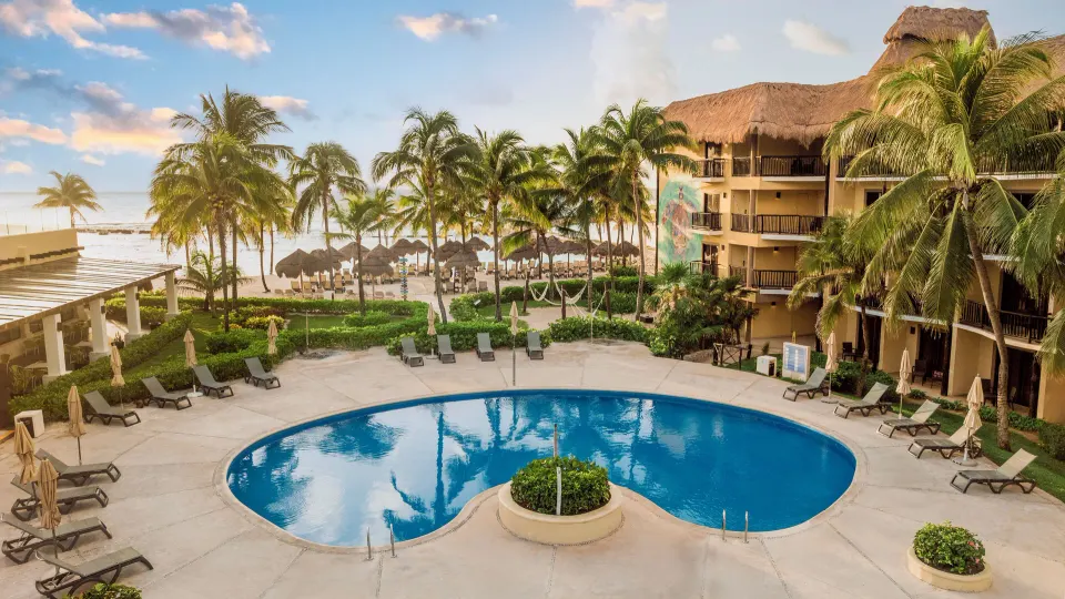 Round resort pool and sunloungers with palm trees at Catalonia Yucatan Beach.