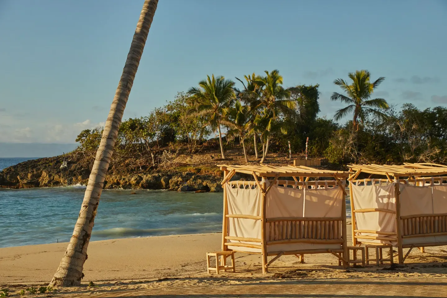 Bamboo cabanas sit on the beach beside a rocky palm-covered point at Cayo Levantado Resort.