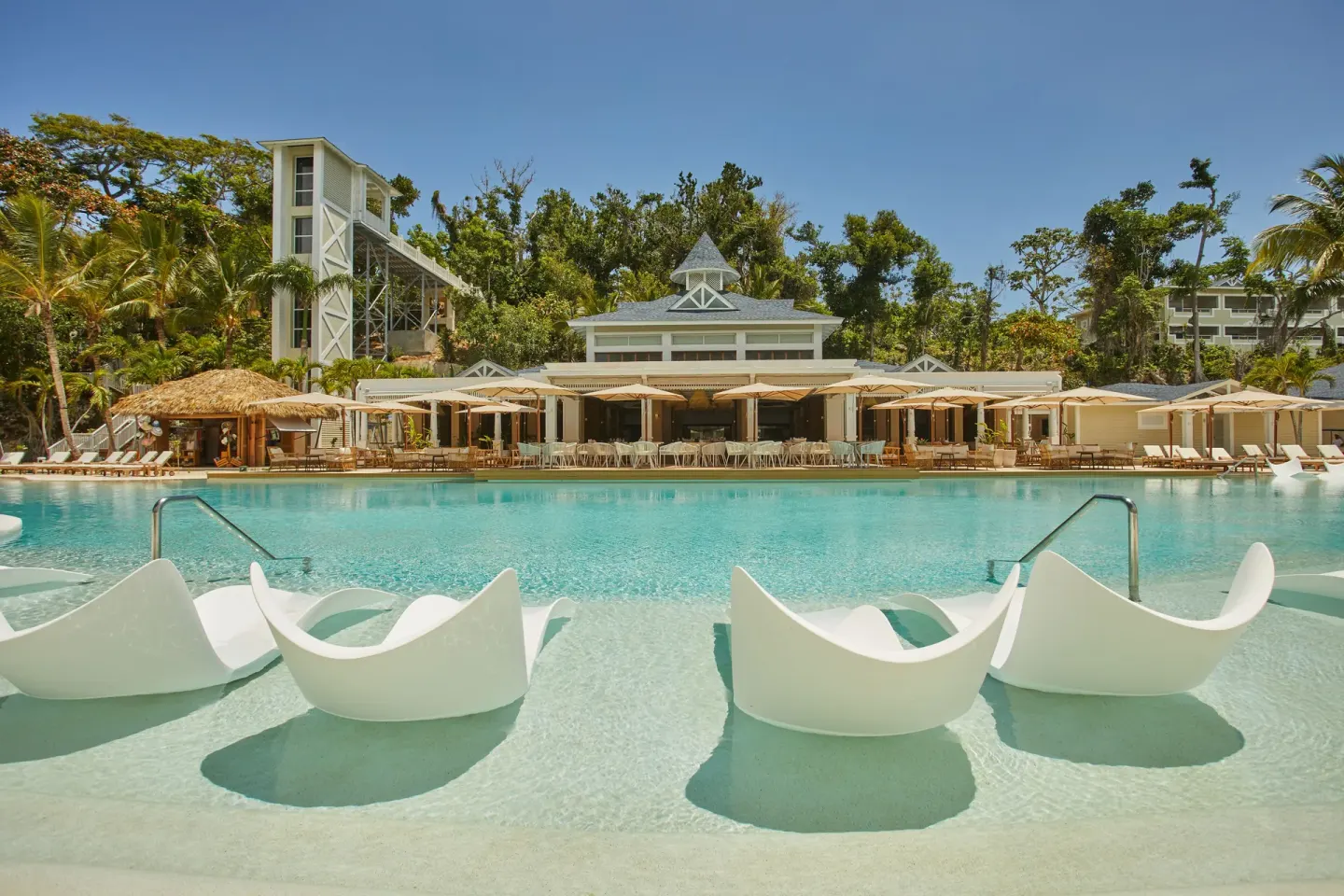 In-water lounge chairs face the main pool and resort buildings at Cayo Levantado Resort.