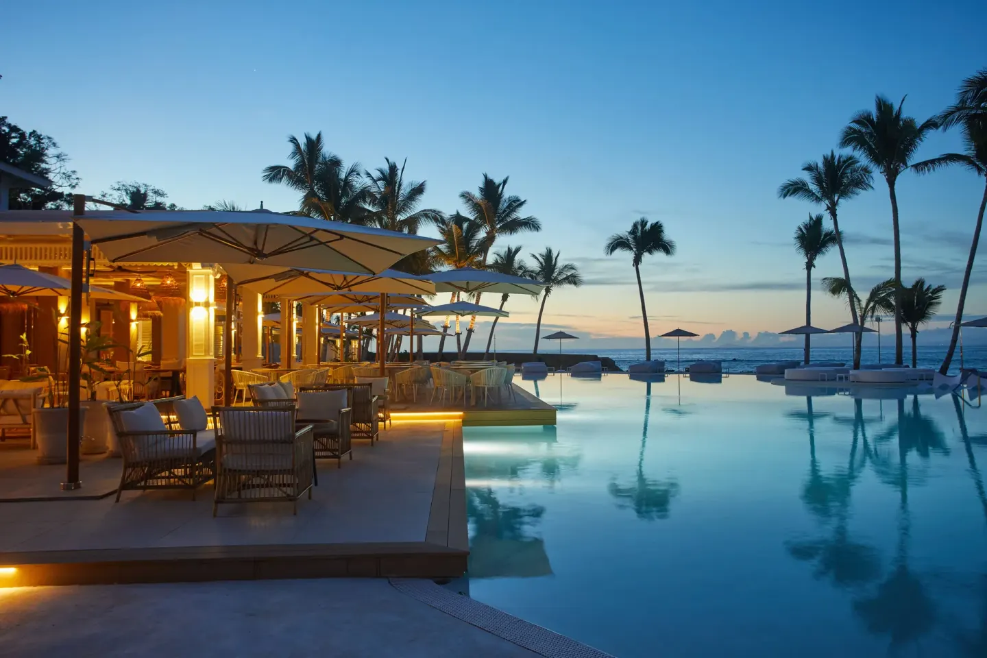 Infinity pool at dusk with terrace seating and palm silhouettes at Cayo Levantado Resort.