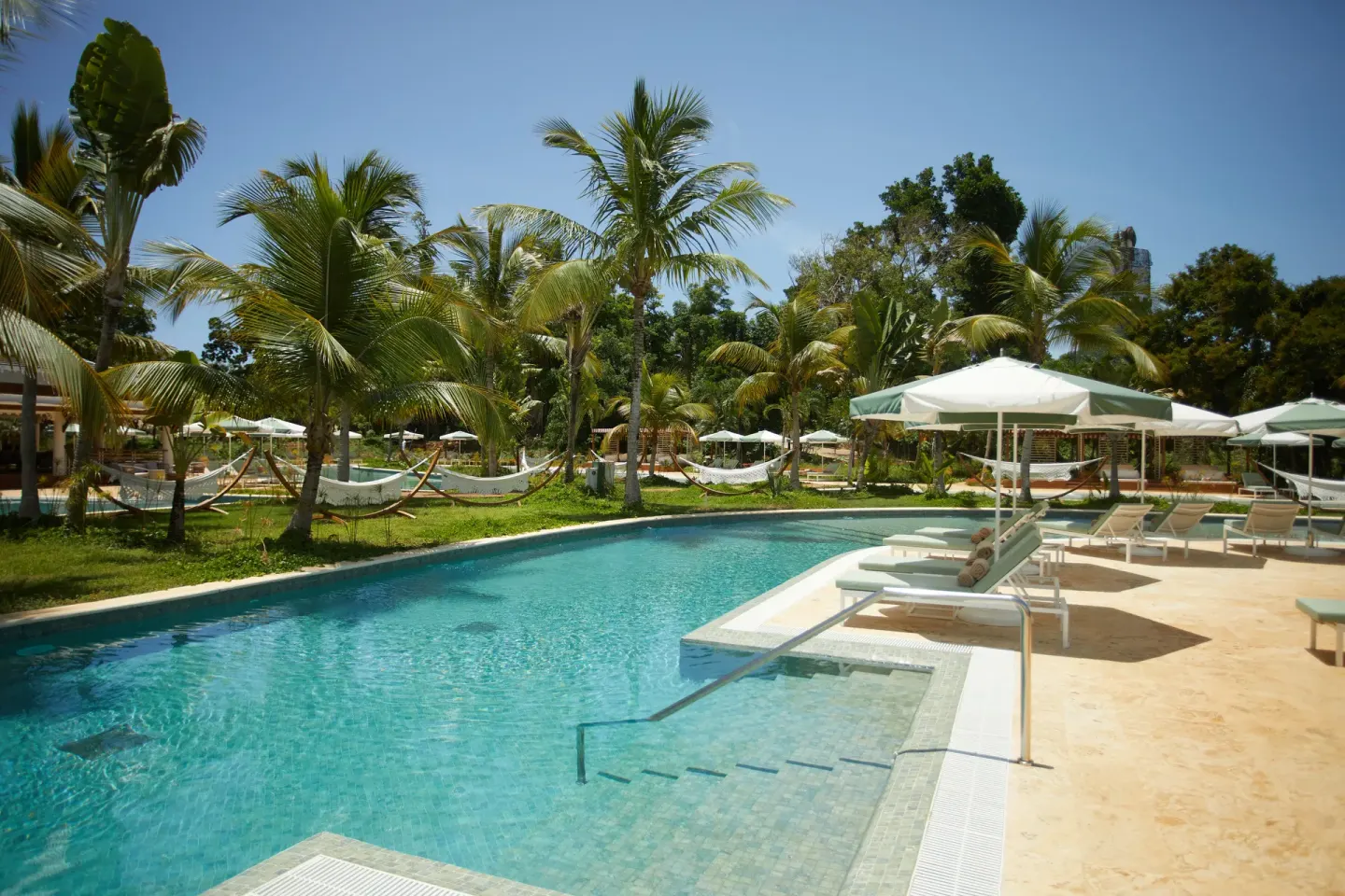 A pool with loungers, umbrellas, hammocks, and palms at Cayo Levantado Resort.