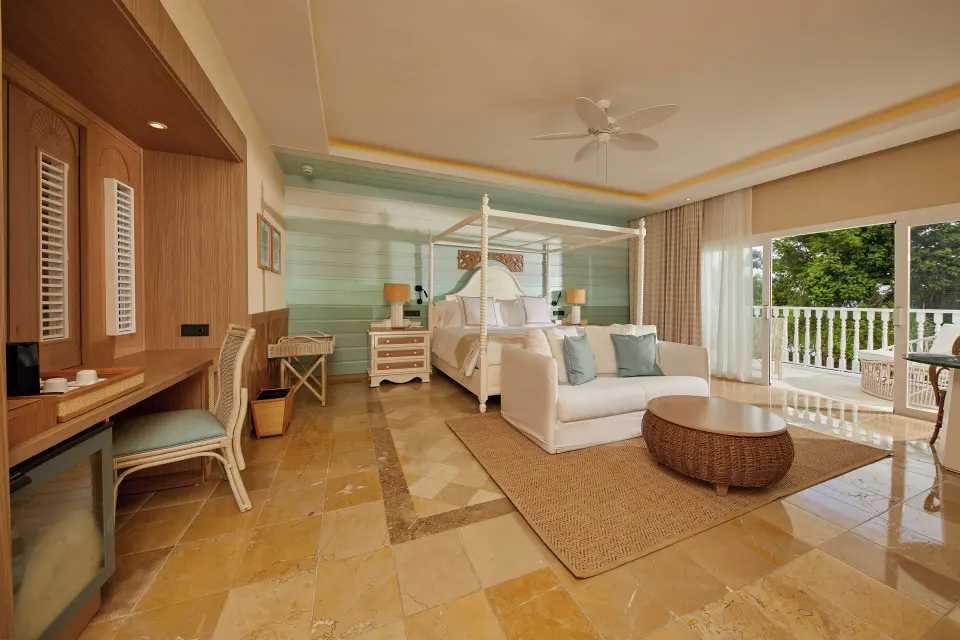 Junior Suite king bed, sofa, desk, and balcony doors at Cayo Levantado Resort.