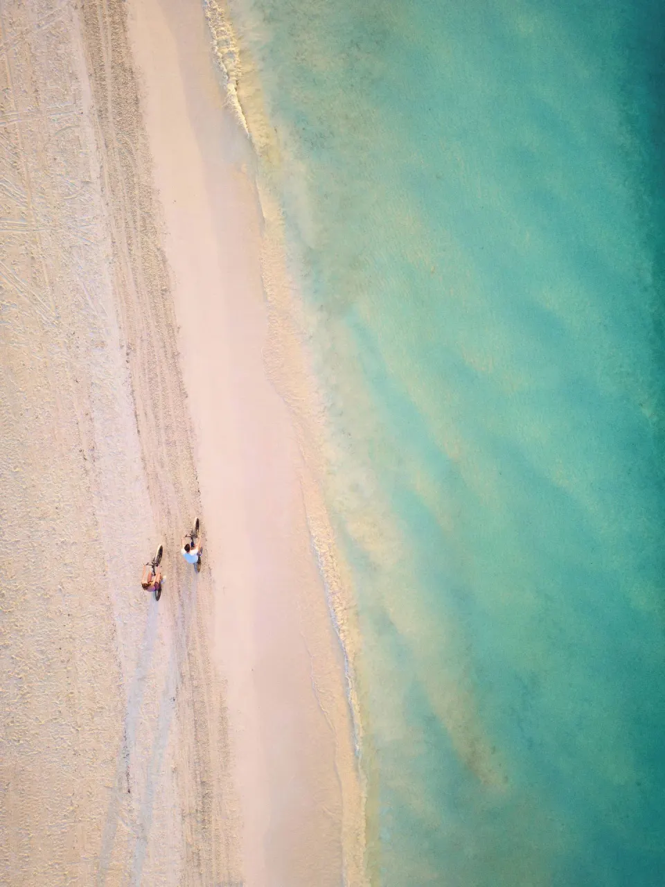 Aerial view of two people walking bikes beside turquoise water at Chablé Maroma.