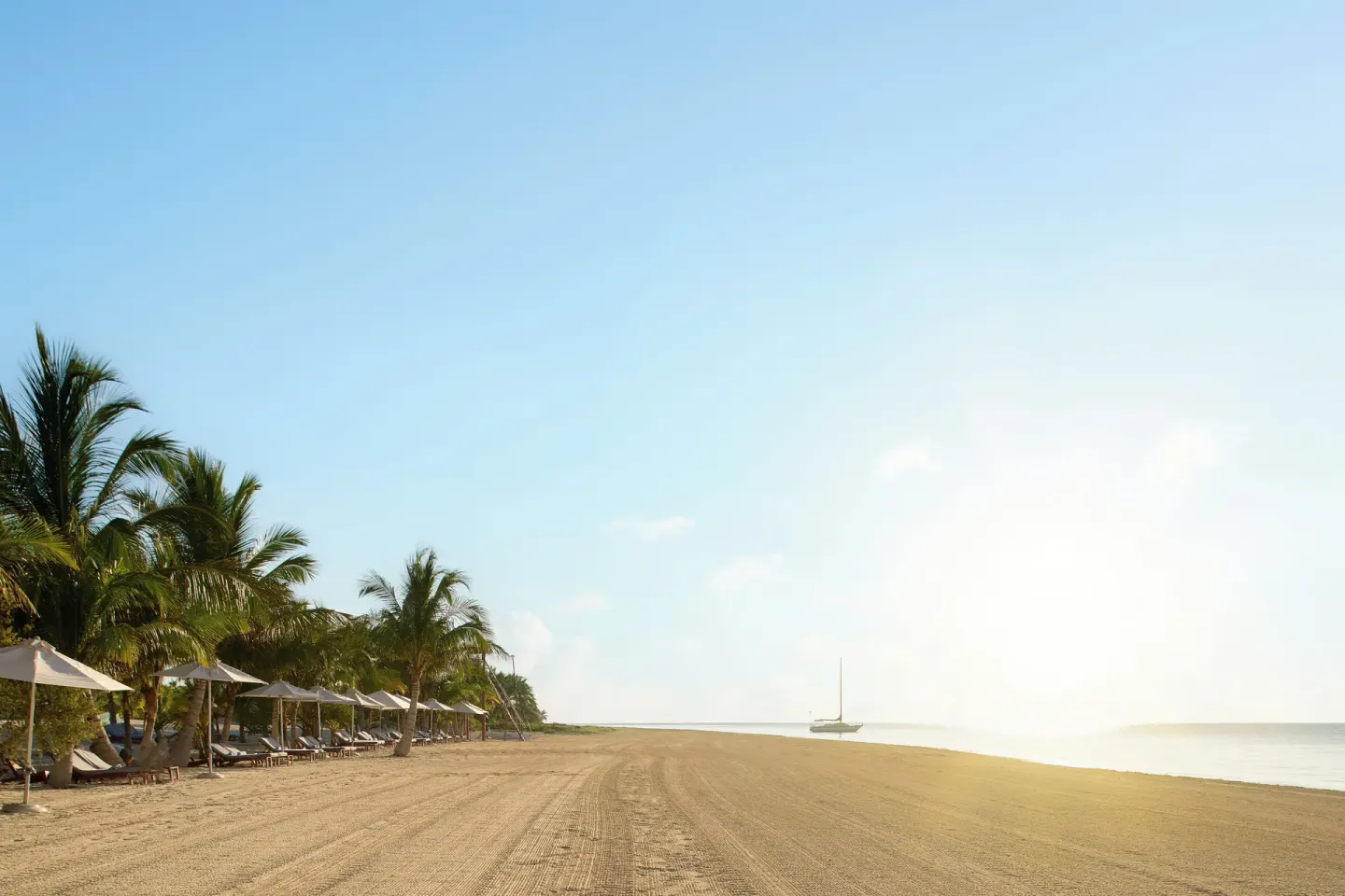 Wide sandy beach with palms, loungers, umbrellas and a sailboat at Chablé Maroma.