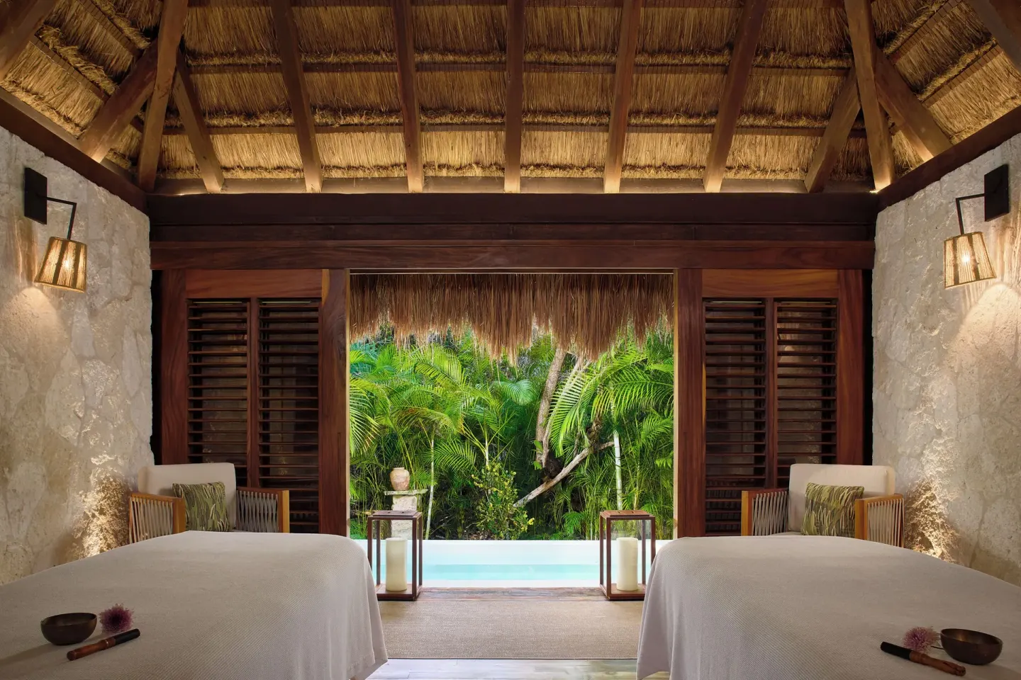 Spa treatment room with two massage beds and greenery outside at Chablé Maroma.