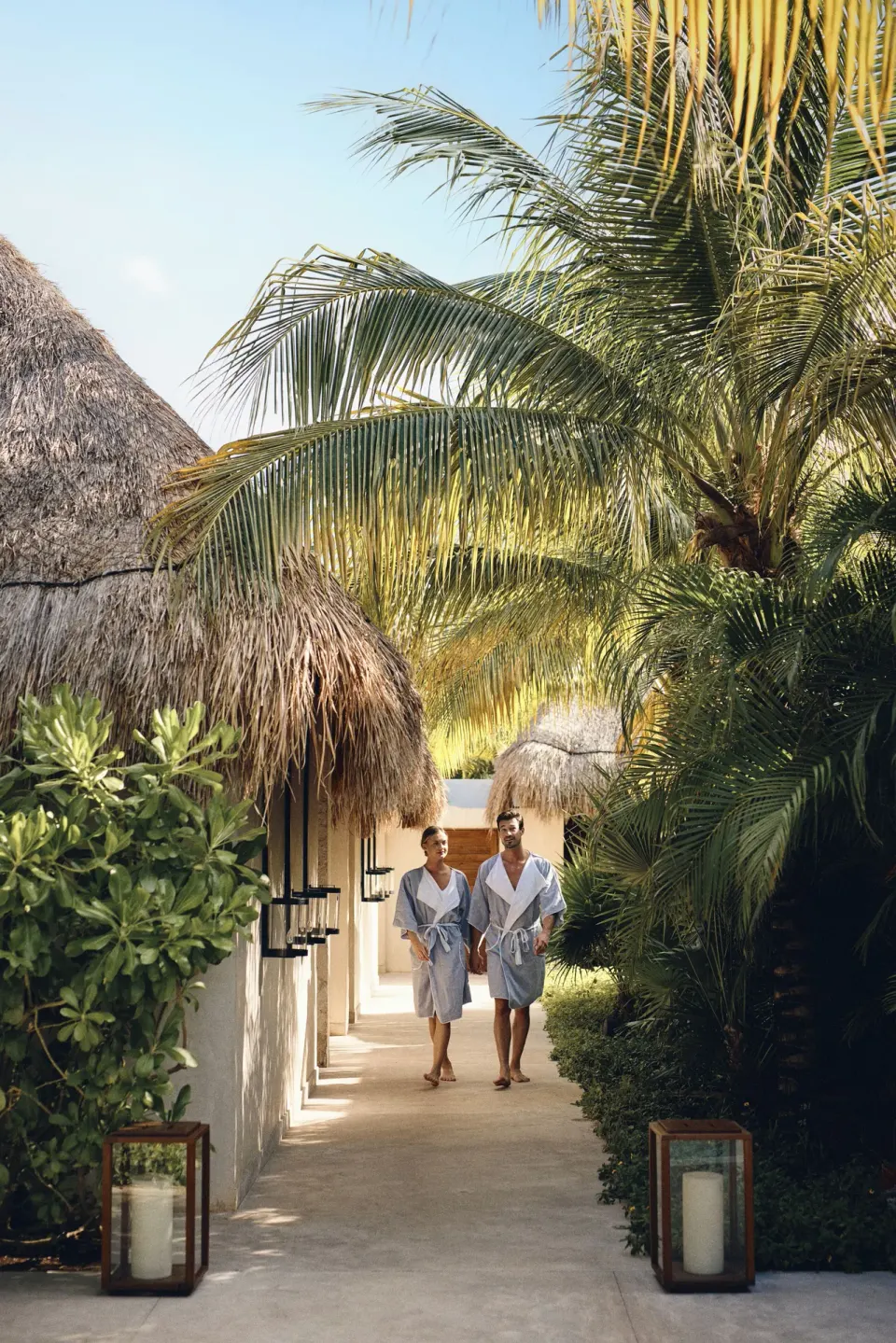 Two guests in robes walking along a palm-lined pathway at Chablé Maroma.