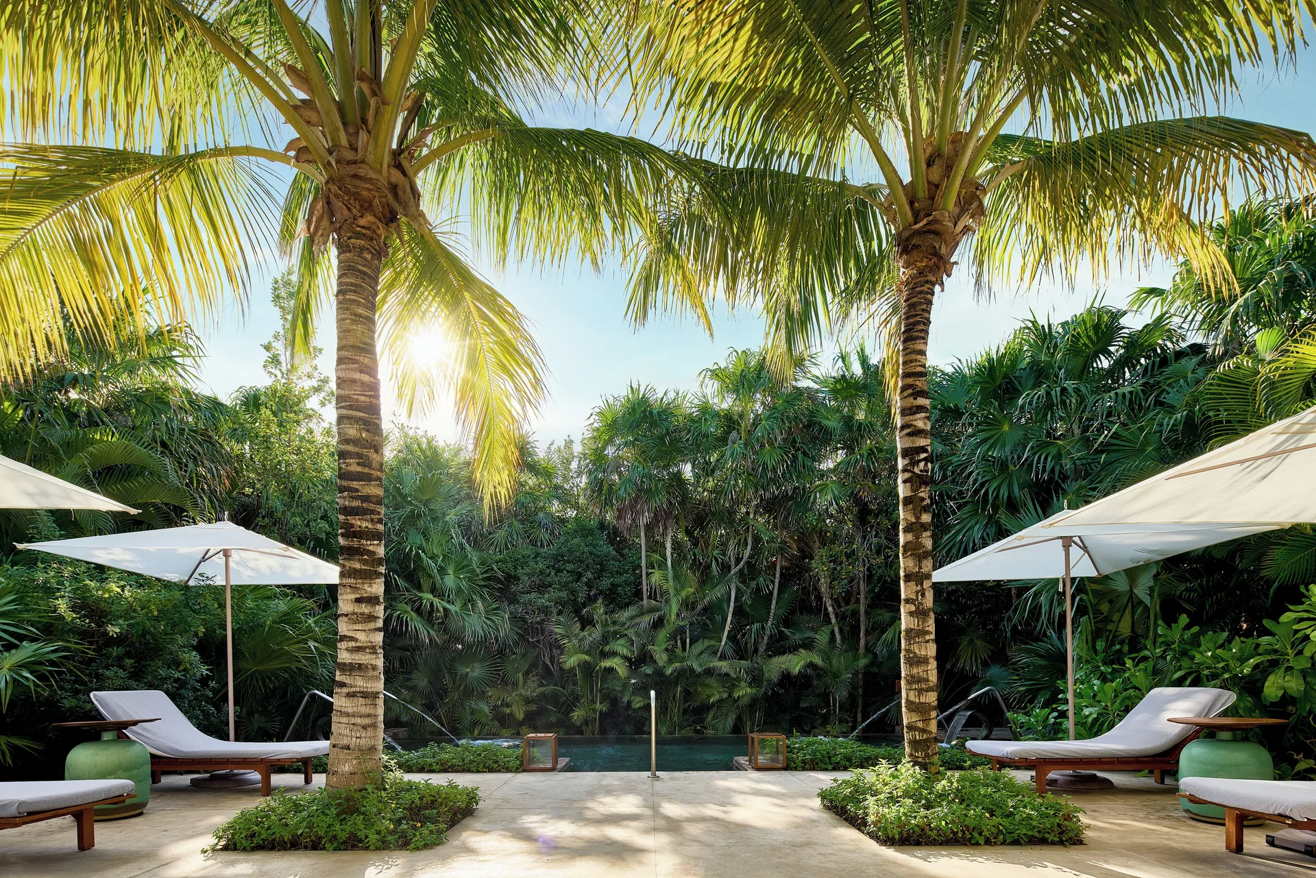 Palm-shaded loungers and umbrellas beside a small pool at Chablé Maroma.