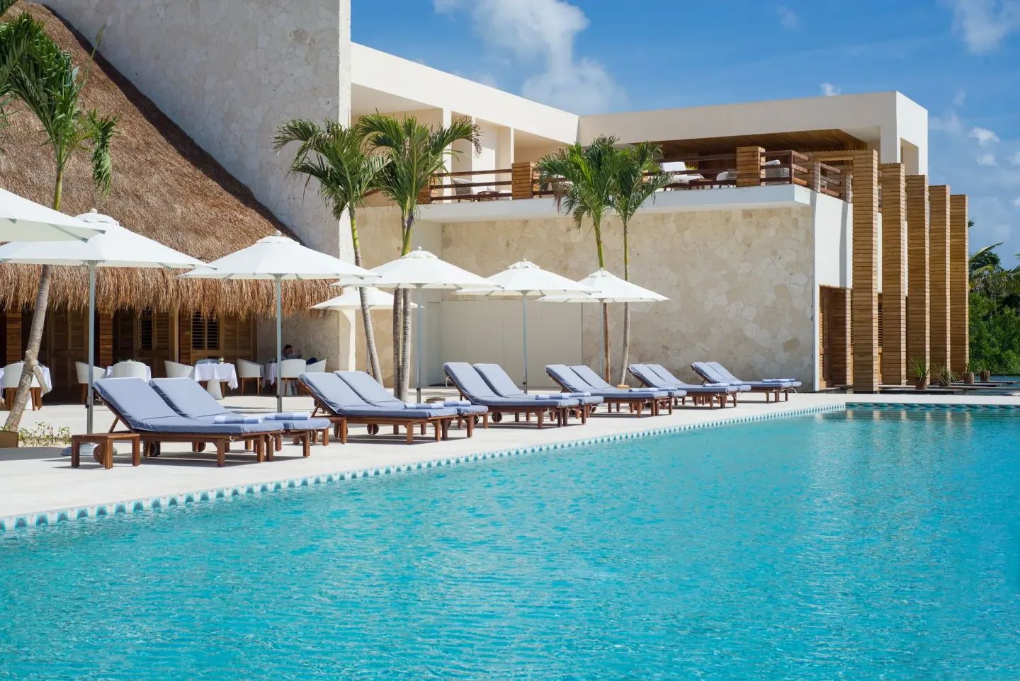 Pool deck with loungers, umbrellas, palms, and resort buildings at Chablé Maroma.