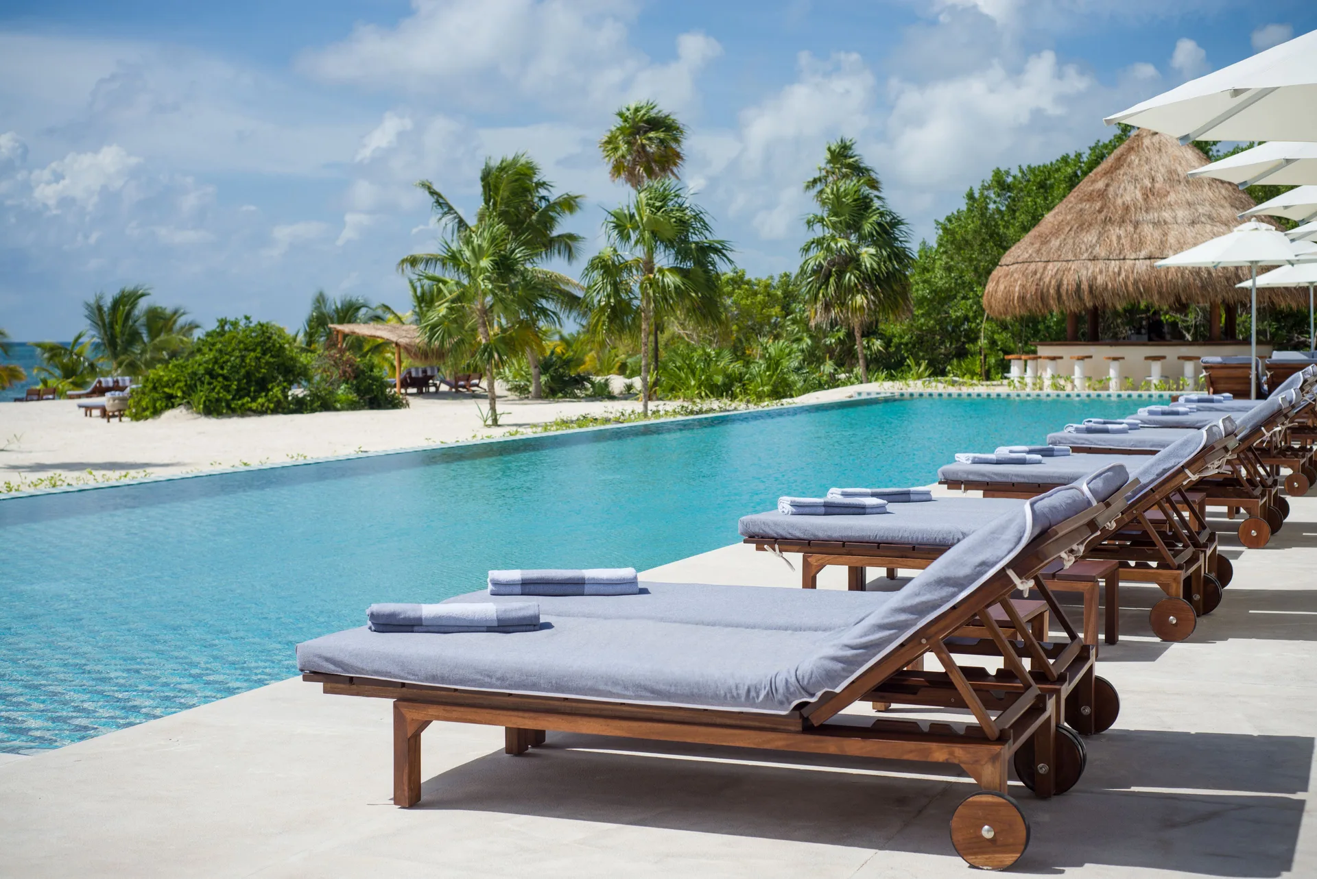 Row of cushioned loungers beside the pool and palms at Chablé Maroma.